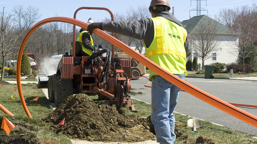 Two installers work together to install conduit for fiber optic cable.